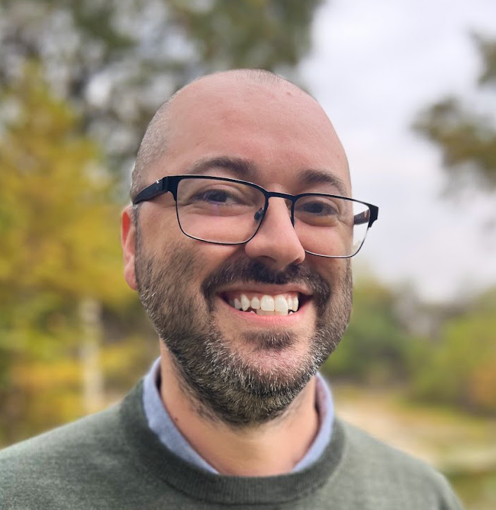 A nerdy, bald programmer with glasses smiling at you like he knows what's going on.